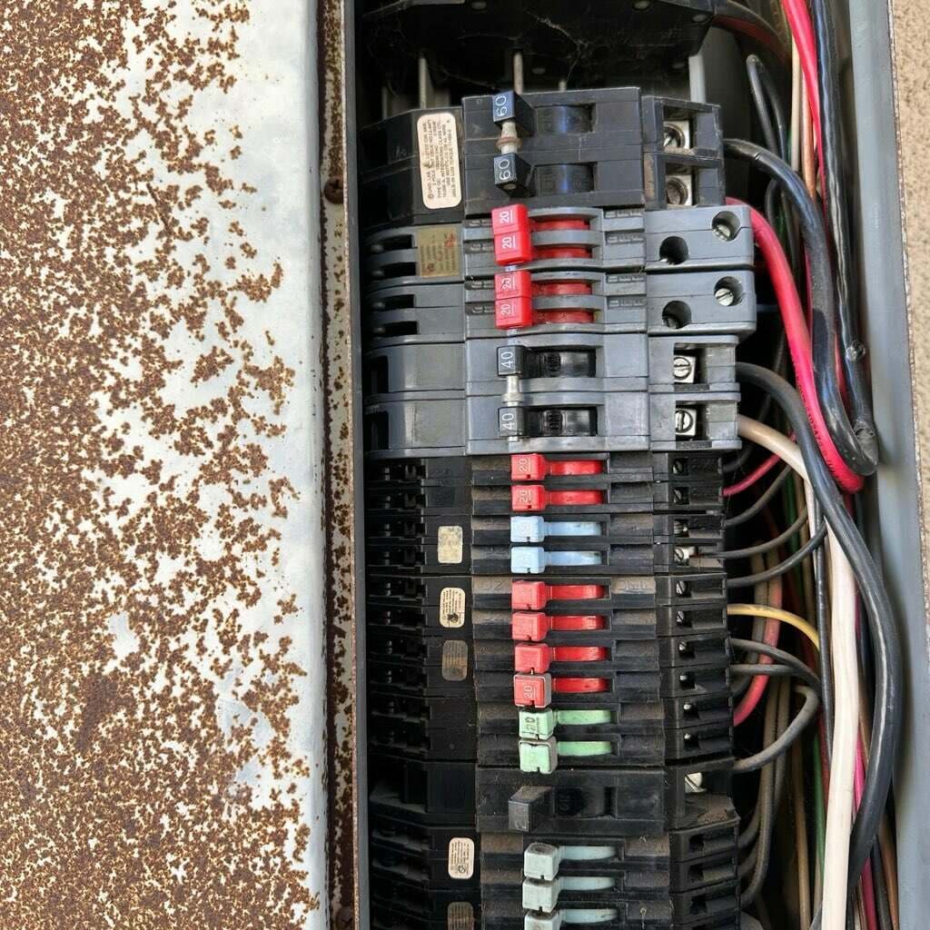 Close-up of outdated residential circuit breaker panel showing rust and worn breakers