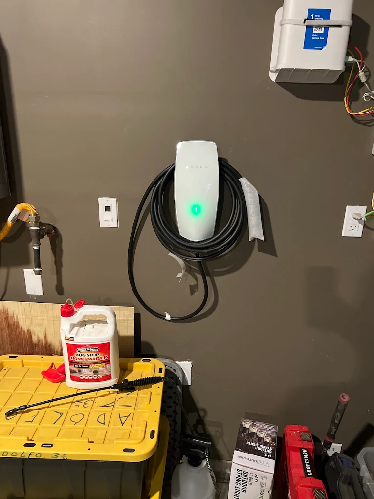 Active Tesla EV Charger with illuminated green status light installed in a residential garage workspace.