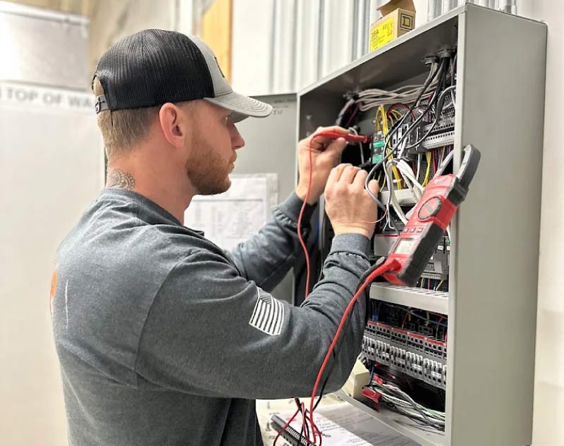 alt="Baker Electric Inc technician diagnosing a commercial electrical panel with a multimeter in Visalia, CA"